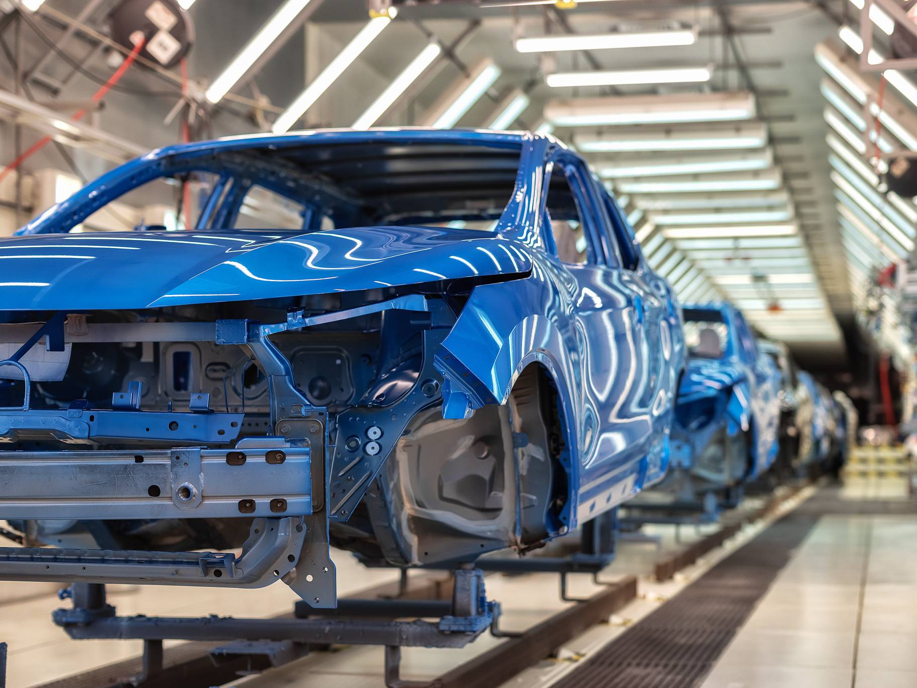 A row of blue car frames on an automotive assembly line in a well-lit factory setting.